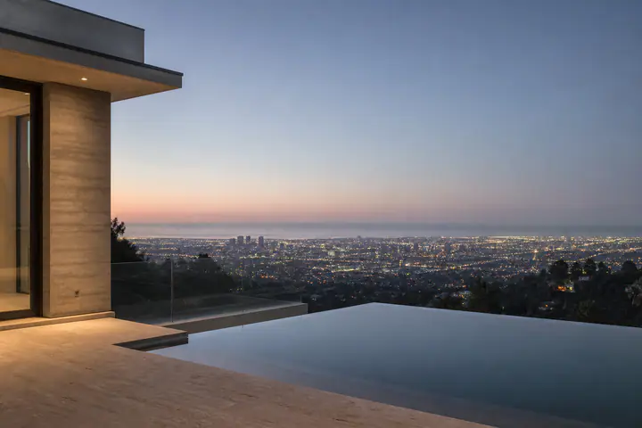 Los Angeles at dusk from a hillside terrace, the city lights coming on below an infinity pool.
