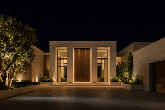 A white contemporary house in Beverly Hills at dusk, a mature tree lit in the motor court