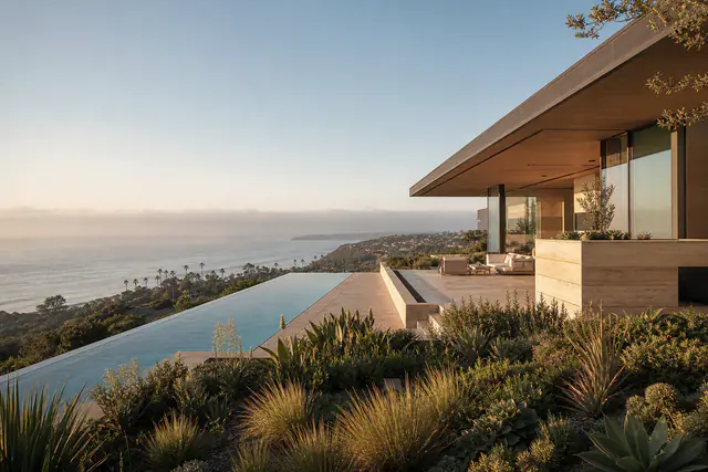 A modern house on a Pacific Palisades bluff at dusk, the coastline lit below