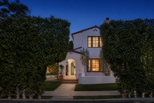 The white stucco facade of 8814 Rosewood Avenue at dusk, lit windows behind a mature ficus hedge