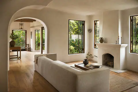 Inside the 8814 Rosewood Avenue sample listing: a plastered living room under a rounded arch, a low sofa facing a stone fireplace, tall steel windows onto the garden.