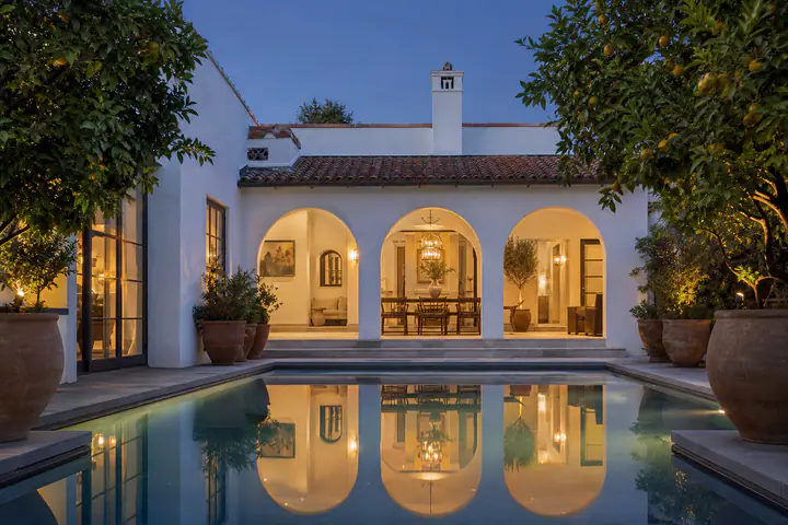 The saltwater pool at 8814 Rosewood Avenue at blue hour, reflecting the arched loggia and the lit casement windows