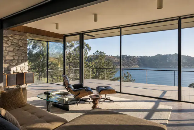 The living room: a stone fireplace wall, glass on three sides, the deck and reservoir beyond.
