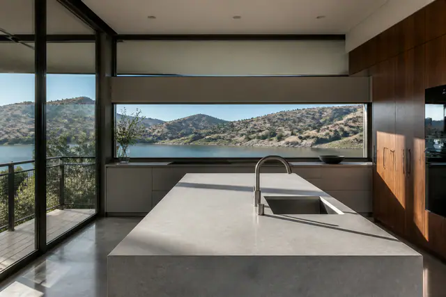 The kitchen: a honed concrete island, walnut cabinetry, a ribbon window over the reservoir.