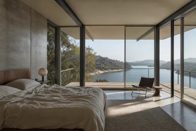 The primary bedroom in a glass corner, a board-formed concrete wall, the deck to the water.